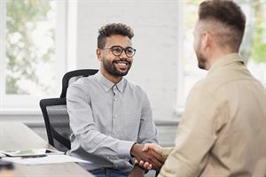 two men in an office setting shaking hands while seated next to a desk