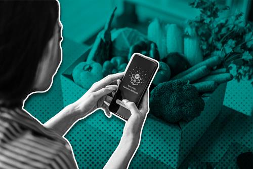 Woman holding phone in front of box of vegetables