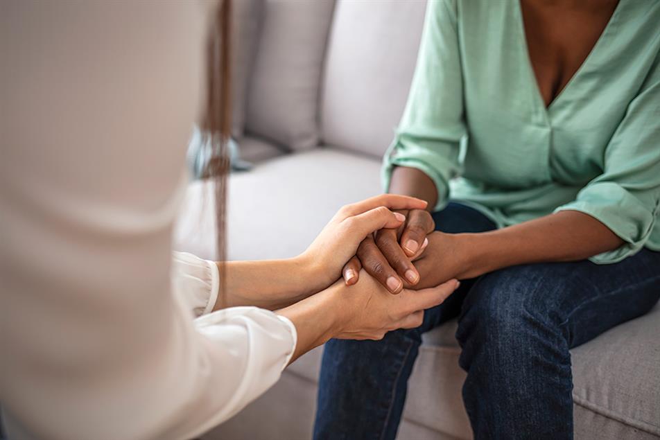 A person giving a supportive hand squeeze to a woman sitting on a sofa