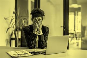 Person sat in front of a laptop with hands over their face