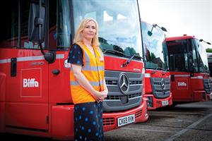 Sarah Airey from Biffa wears a branded high-vis vest over her dress and stands in front of a Biffa lorry