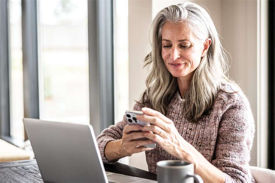 Woman looking at a mobile sat in front of a laptop