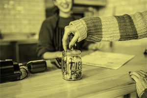 Close up of a hand putting money in a tips jar