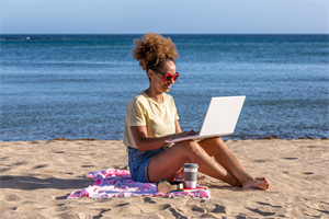 Woman sat on a beach with a laptop