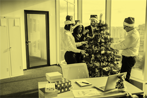 People wearing Santa hats standing around a Christmas tree in an office