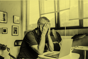 Man sat in front of a laptop with hands over his face