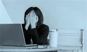 Person sat in front of a laptop with hands over their face