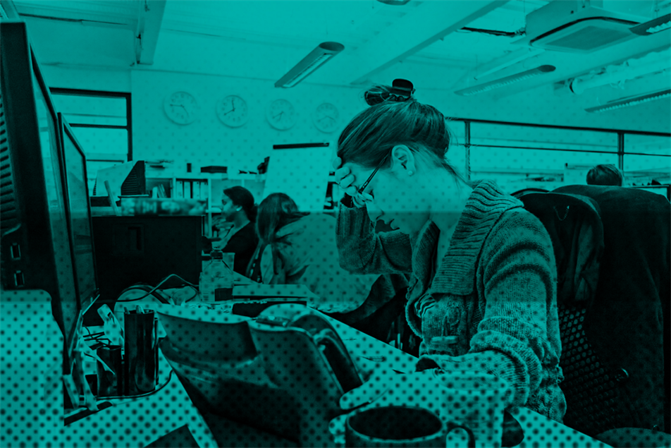 A woman sitting at a desk, with one hand on her head and the other hand reaching towards a phone